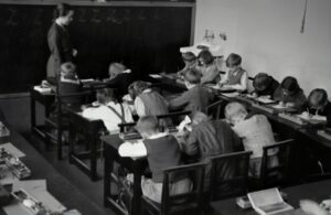 Old black and white photo showing a class room with young children