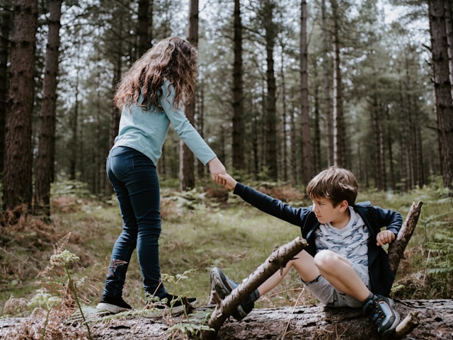 Photo of a young girl, reaching out a hand to help a boy to stand up, after he was fallen.