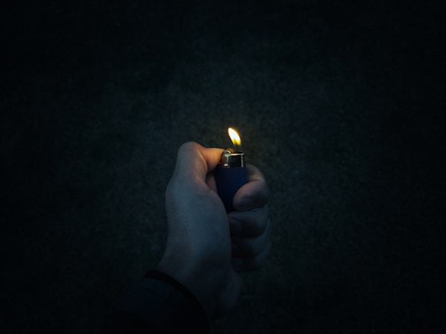 Image of a hand holding a lighted lighter in darkness